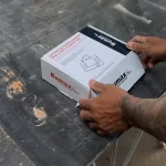 Pessoa segurando uma caixa de suporte de esmerilhadeira para corte em chanfro de 45 graus, ideal para ajustagens precisas em trabalhos de marcenaria e metalurgia.